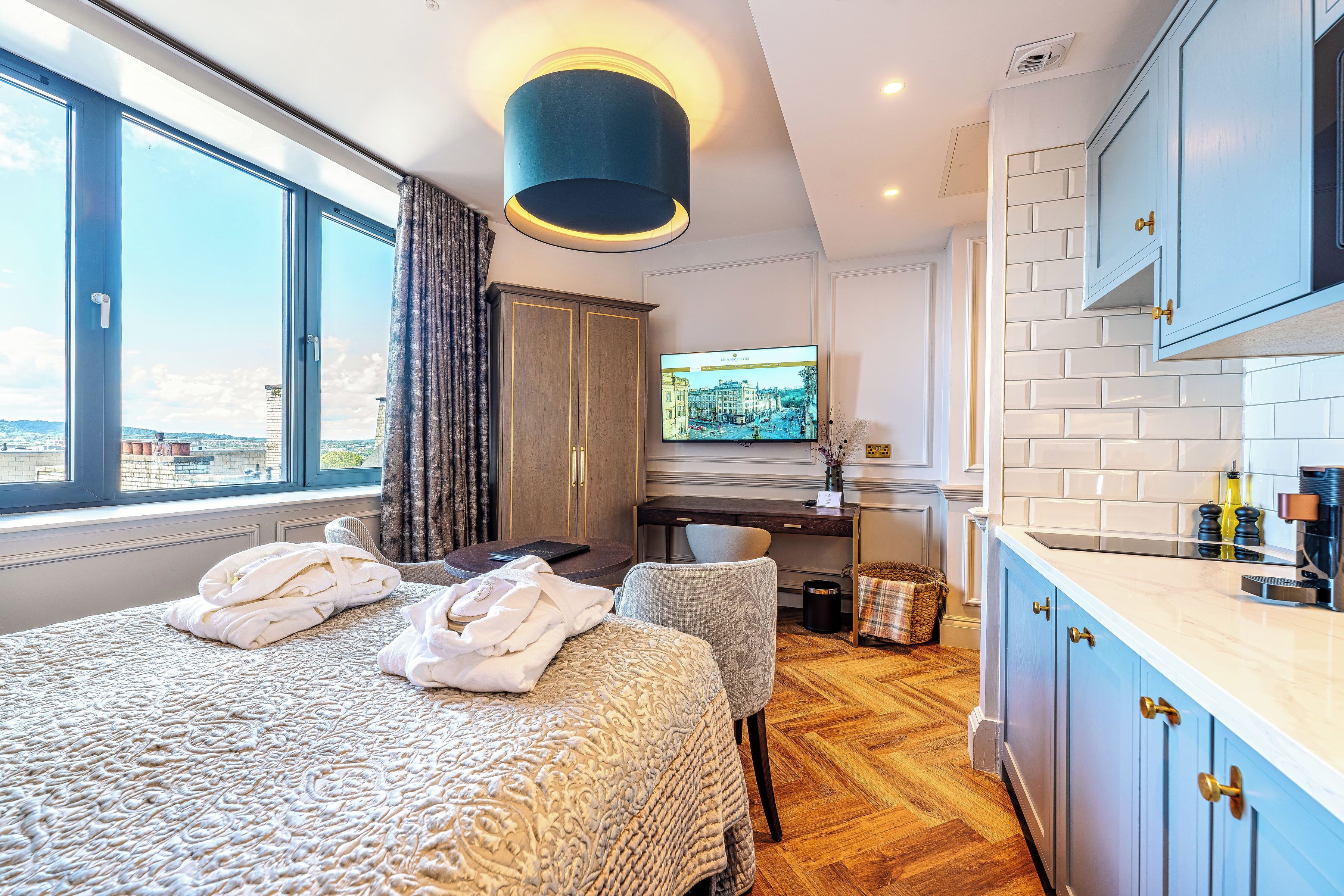 A hotel room with a large bed, a desk with a computer, a TV, and a view of the city.