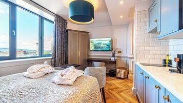 A hotel room with a large bed, a desk with a computer, a TV, and a view of the city.