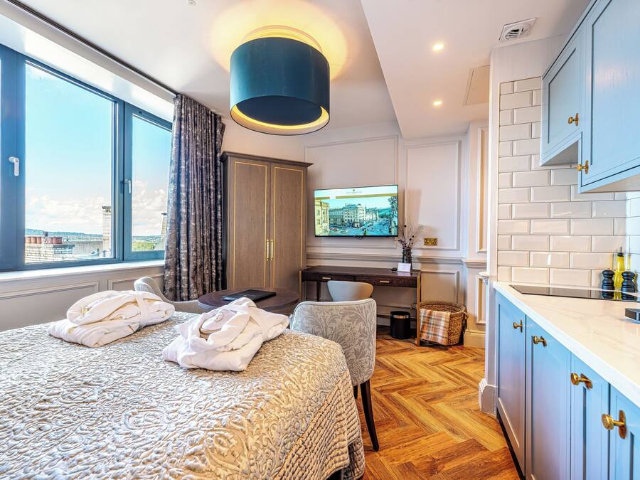 A hotel room with a large bed, a desk with a computer, a TV, and a view of the city.