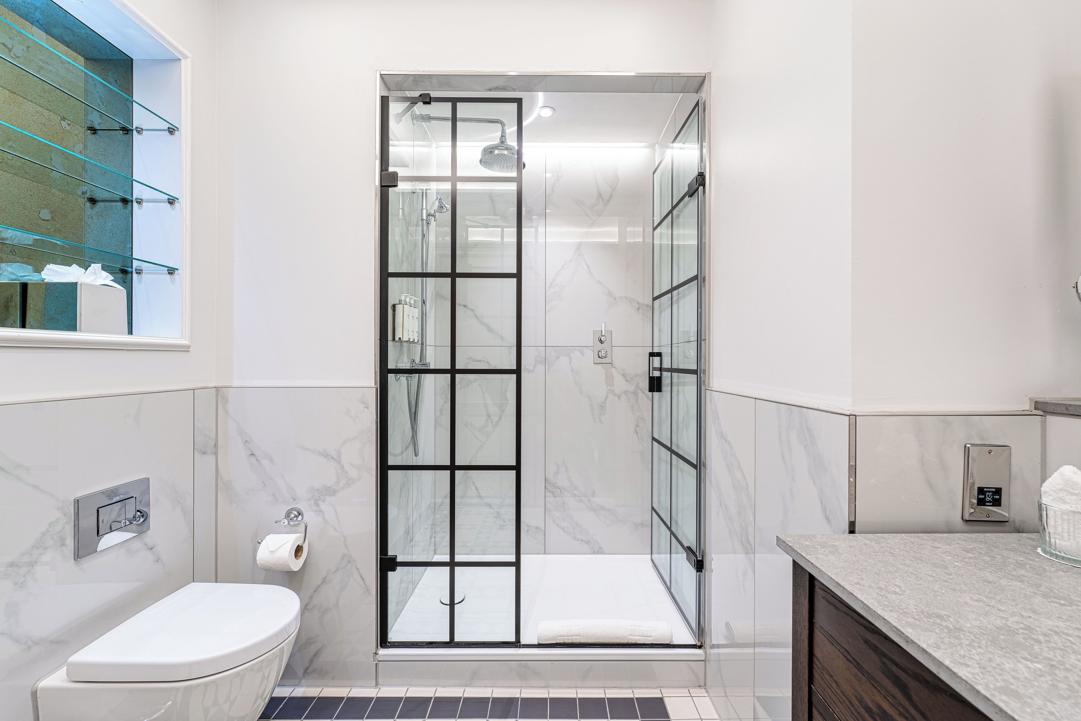 Een moderne badkamer met een glazen douchecabine, een toilet en een wastafel met een marmeren aanrecht.