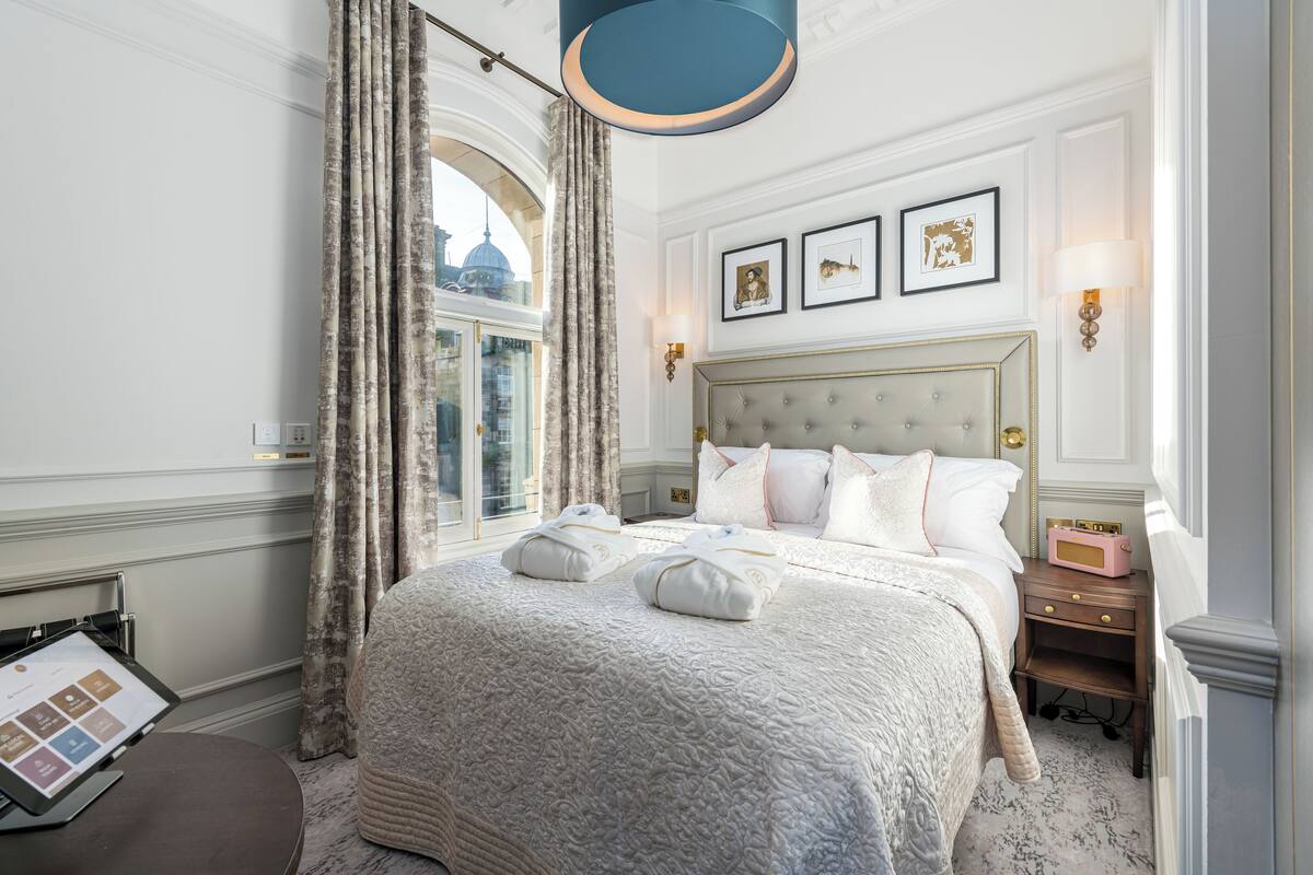 Une chambre d’hôtel avec un grand lit, une table de chevet, une lampe et une vue sur le paysage urbain par la fenêtre.