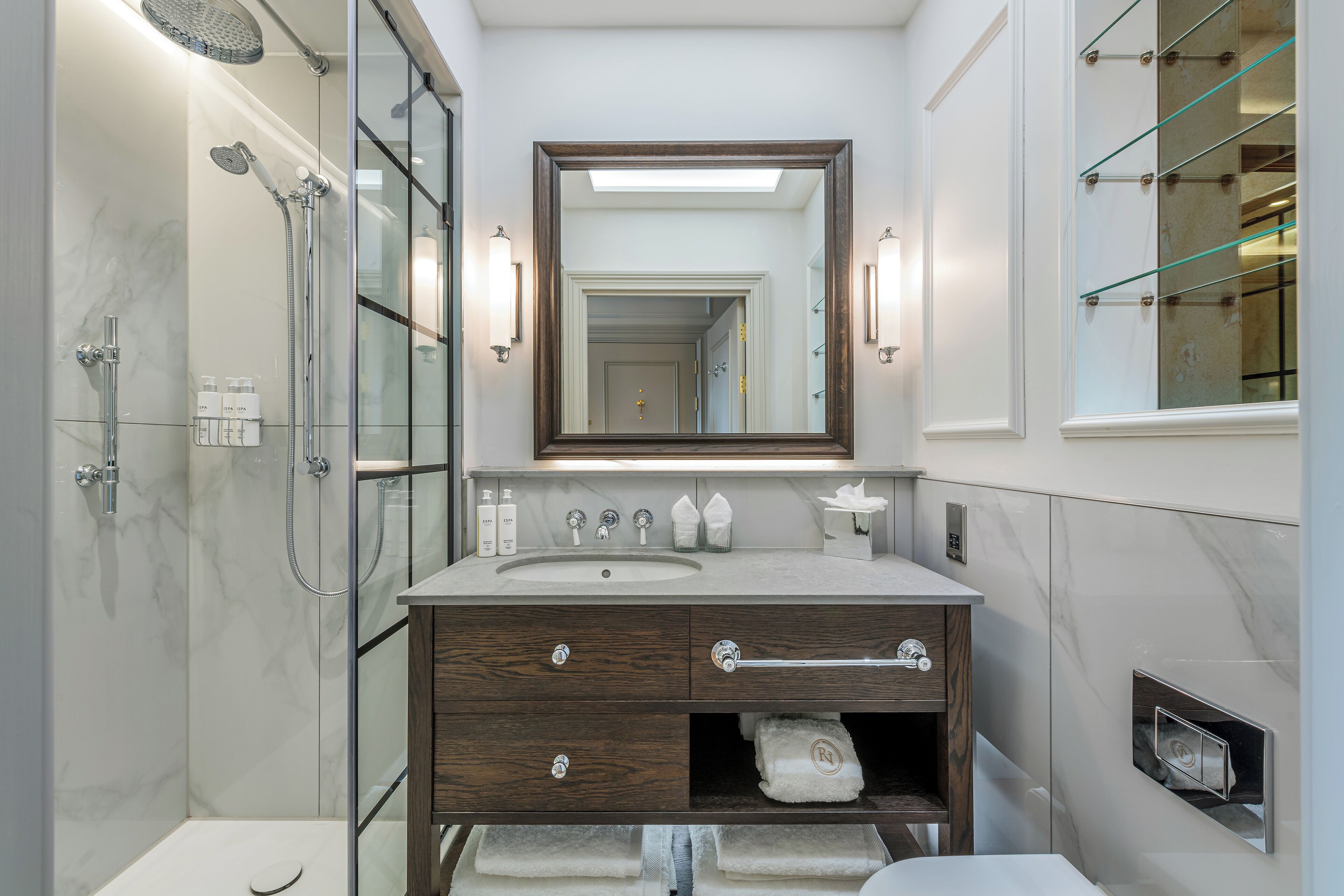 Une salle de bain moderne avec une douche à parois de verre, un lavabo en marbre et un meuble-lavabo en bois doté de tiroirs.