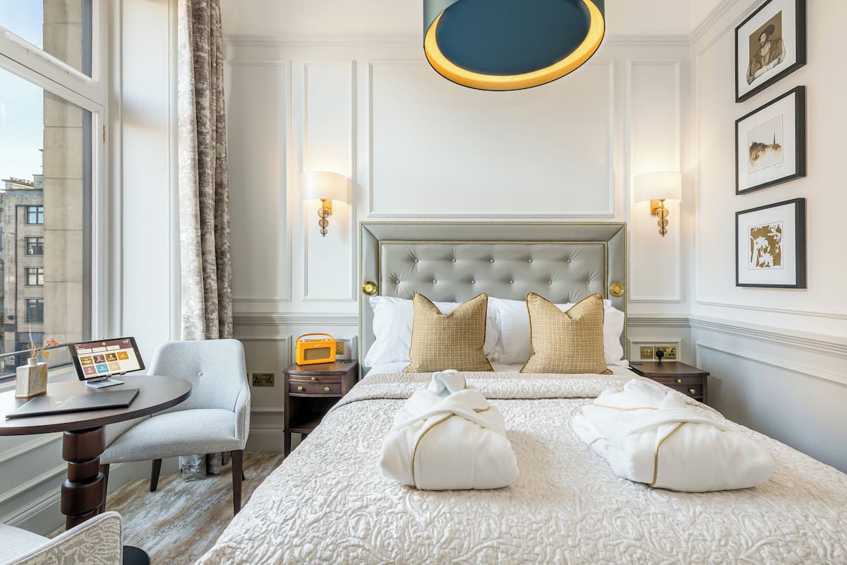 Une chambre d’hôtel avec un grand lit, un bureau avec un ordinateur, une chaise et une vue sur la ville par la fenêtre.