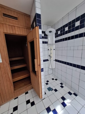 Una sauna con puerta de madera, suelo de baldosas blancas y pared con azulejos azules.