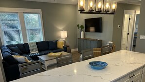 Een moderne keuken met een marmeren aanrecht, een zithoek met een bank en tafel, en een televisie boven de open haard.