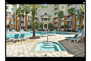 A hotel pool area with multiple pools, lounge chairs, and palm trees.