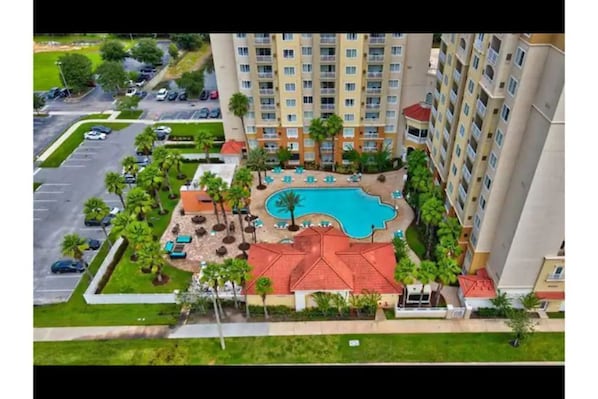 A high-rise hotel with a swimming pool, outdoor seating, and a parking lot.