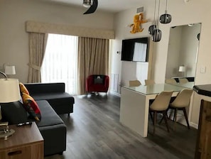 A modern hotel room with a living area, a dining table, and a TV mounted on the wall.