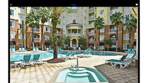A pool area with multiple pools and lounge chairs, surrounded by a multi-story building with balconies. - Universal-Disney Dream 2 Bedroom (Orlando)