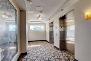 Corredor de hotel com piso estampado, ventilador de teto e elevador.