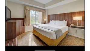 A hotel room with a large bed, a TV, a desk, and a window with curtains. - Universal-Disney Dream 2 Bedroom (Orlando)