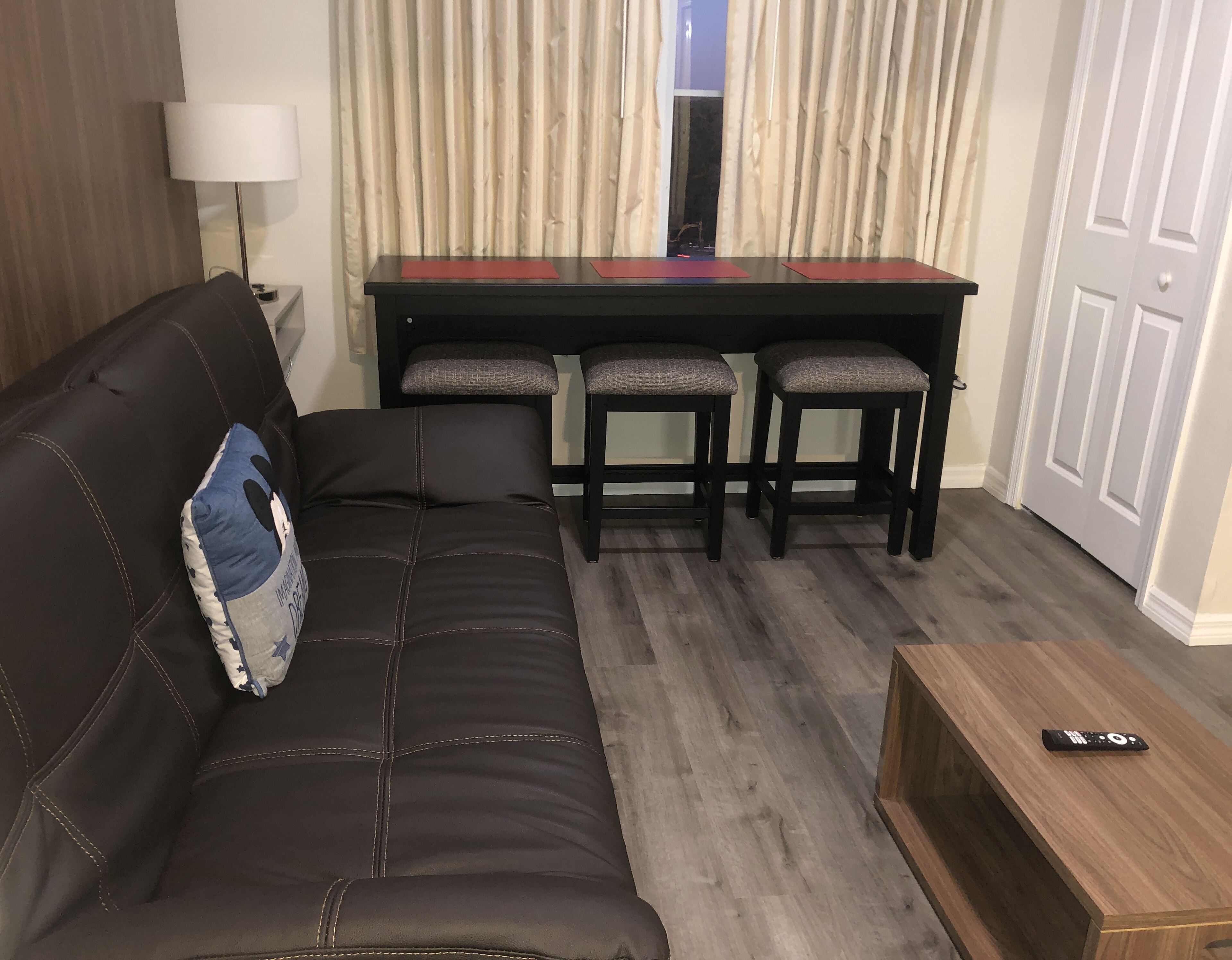 Una sala de estar con un sofá de cuero marrón oscuro, dos sillones a juego, una mesa de centro de madera, una lámpara y una puerta.