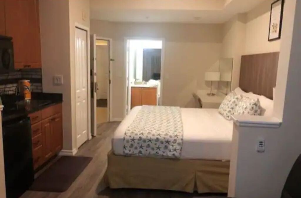 Ein Hotelzimmer mit Bett, Schreibtisch, Stuhl, Spiegel und einer Küchenzeile.
