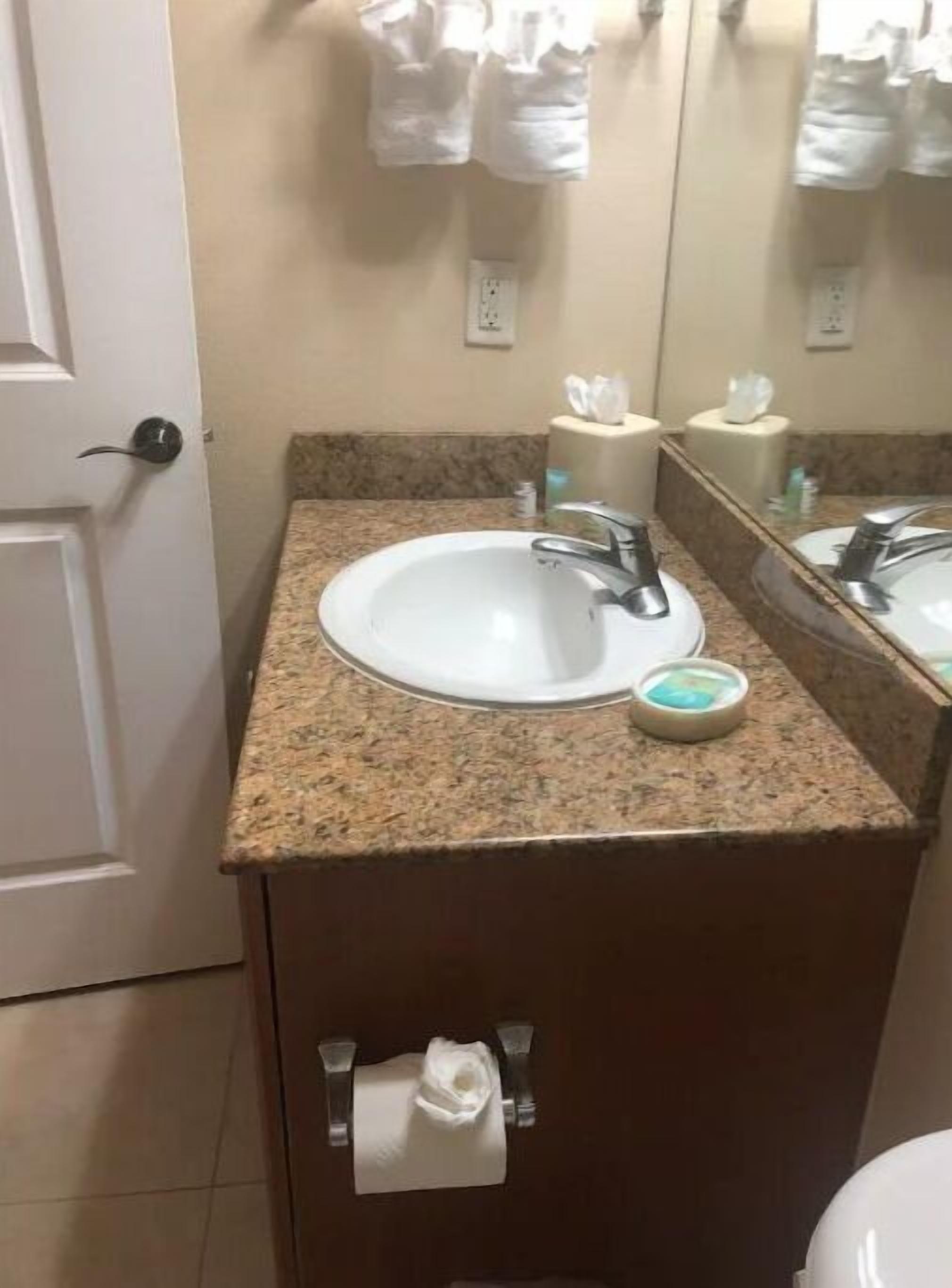 A bathroom with a white sink, a mirror, and a towel hanging on the door.