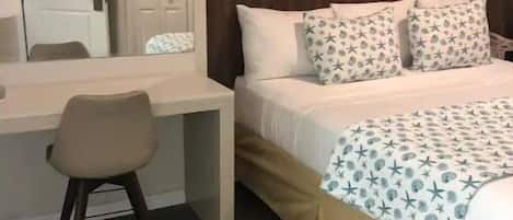 Une chambre d’hôtel avec un bureau en bois, une chaise, un lit agrémenté d’oreillers à motifs et un tableau encadré au mur.