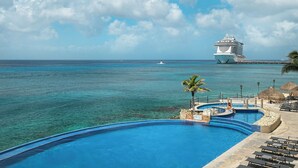Piscina de resort com vista para o oceano e um cruzeiro ao longe.