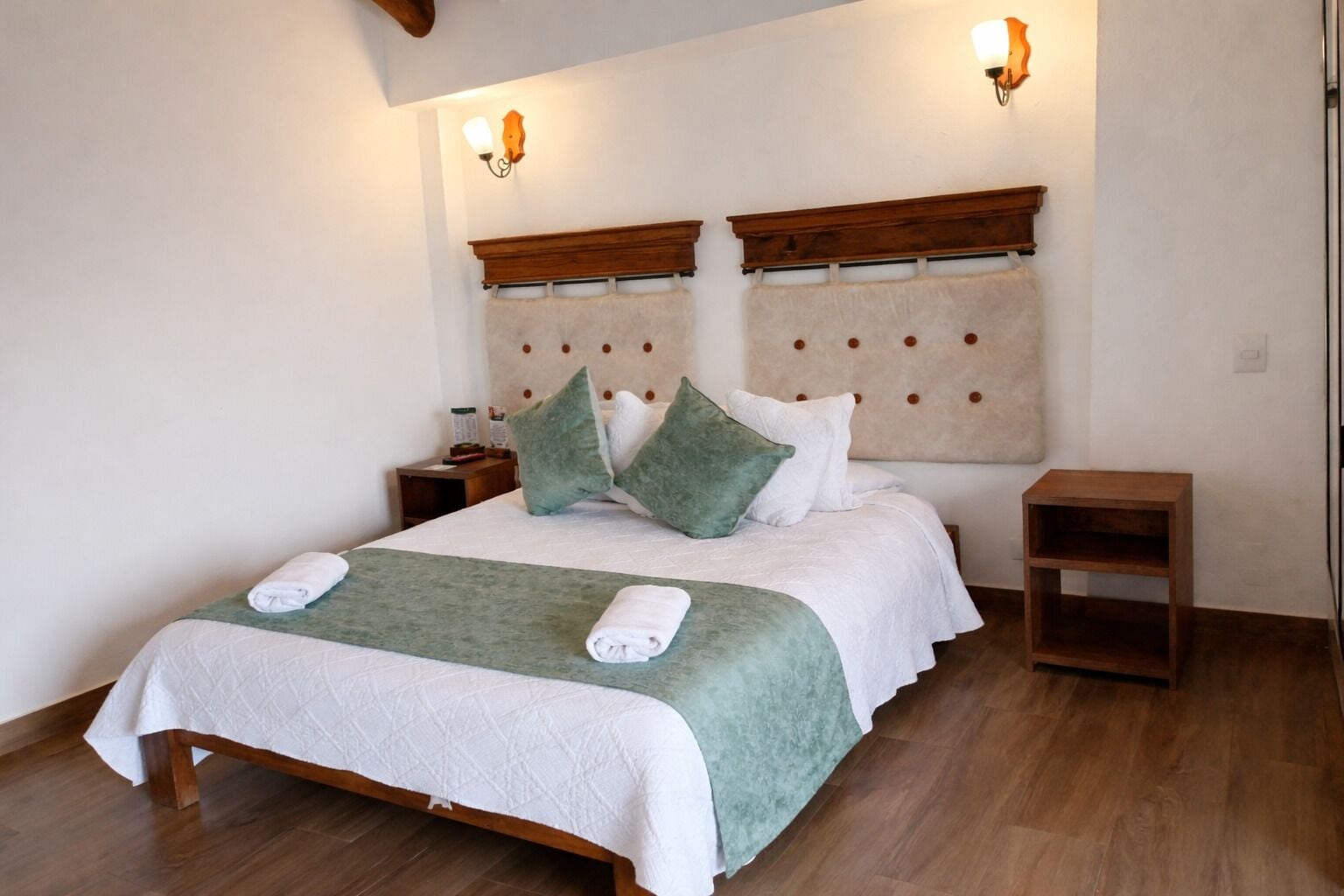 A bed with a wooden frame, a green throw, and white bedding. There are two bedside tables with lamps.