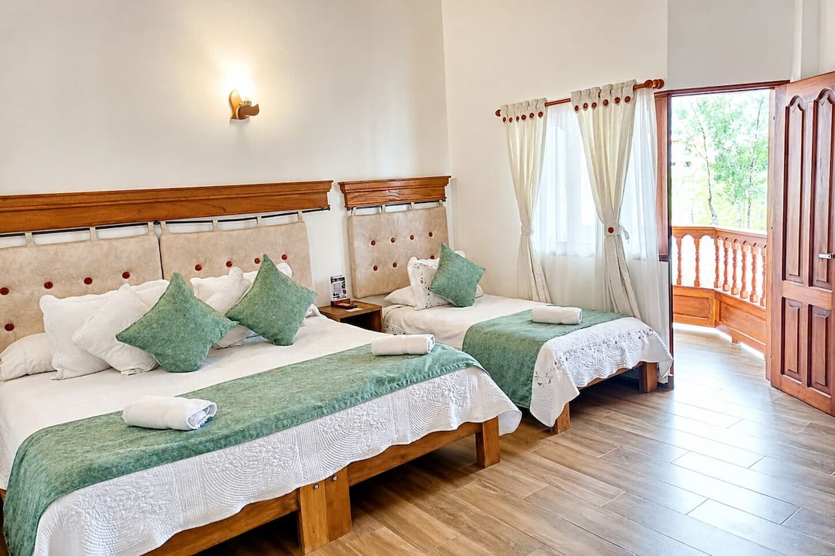 Ein Doppelzimmer mit zwei Betten, Holz-Kopfteilen, einem Nachttisch, einer Wandleuchte und einem Balkon mit Holzbalkon.