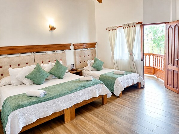 Une chambre double avec deux lits, des têtes de lit en bois, une table de chevet, une lampe fixée au mur et un balcon avec une balustrade en bois.