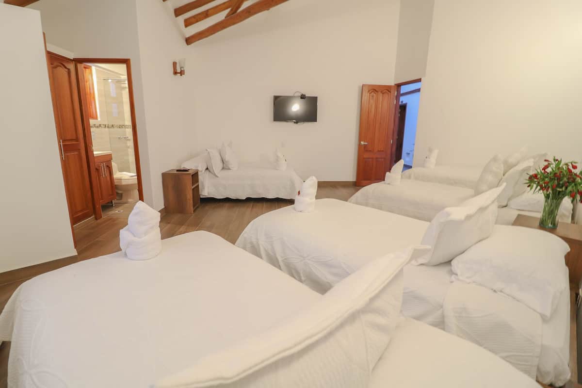 Ein Hotelzimmer mit drei Betten, einem Fernseher und einem durch eine geöffnete Tür einsehbaren Badezimmer.