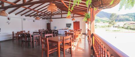 A spacious dining area with wooden tables and chairs, a balcony with a wooden railing, and hanging plants.