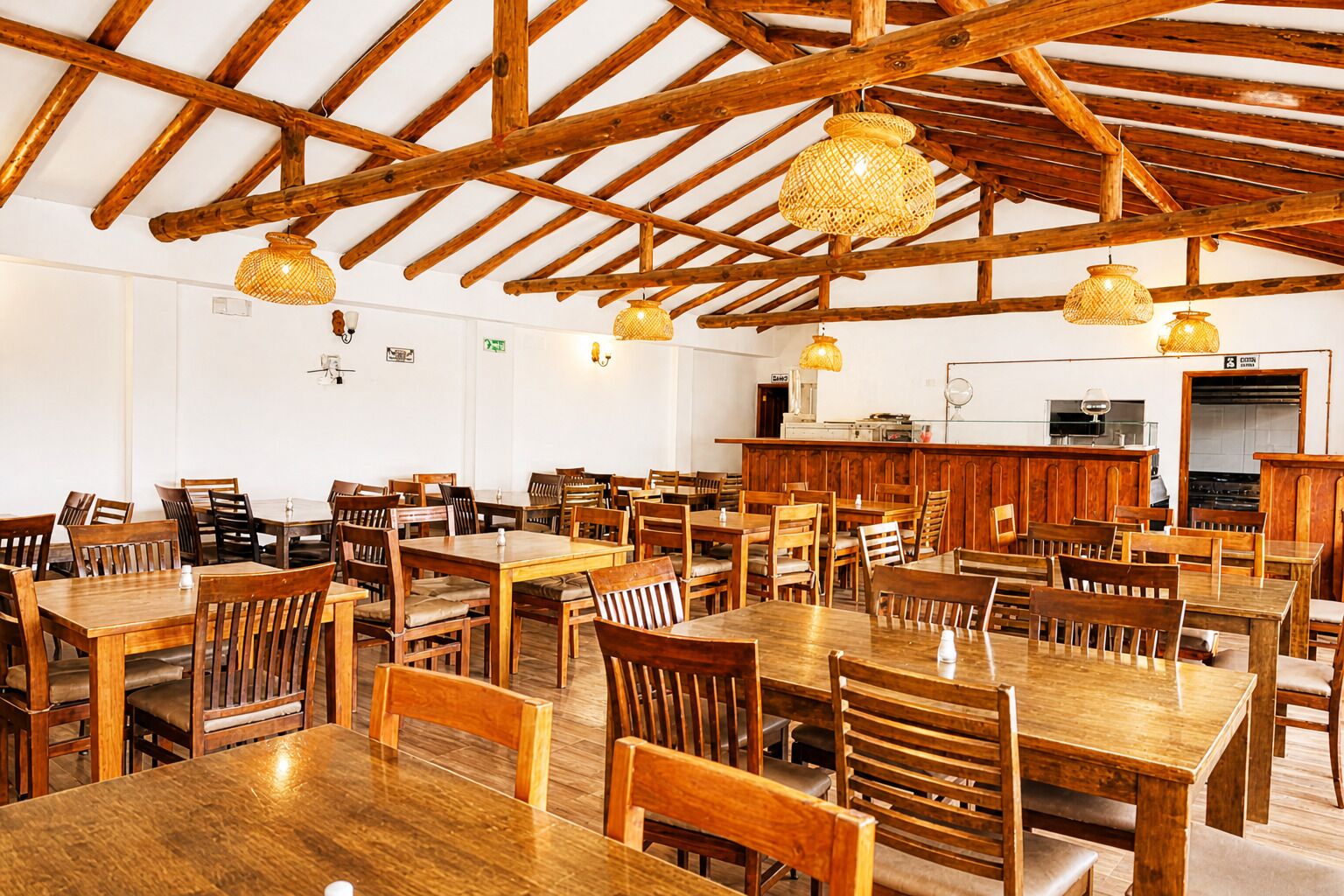 A spacious dining area with wooden tables and chairs, a bar area, and a high wooden ceiling with exposed beams.