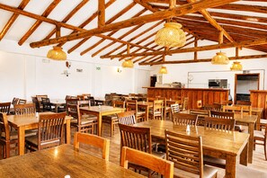 A spacious dining area with wooden tables and chairs, a bar area, and a high wooden ceiling with exposed beams. - Hotel las Palmas (Villa de Leyva)