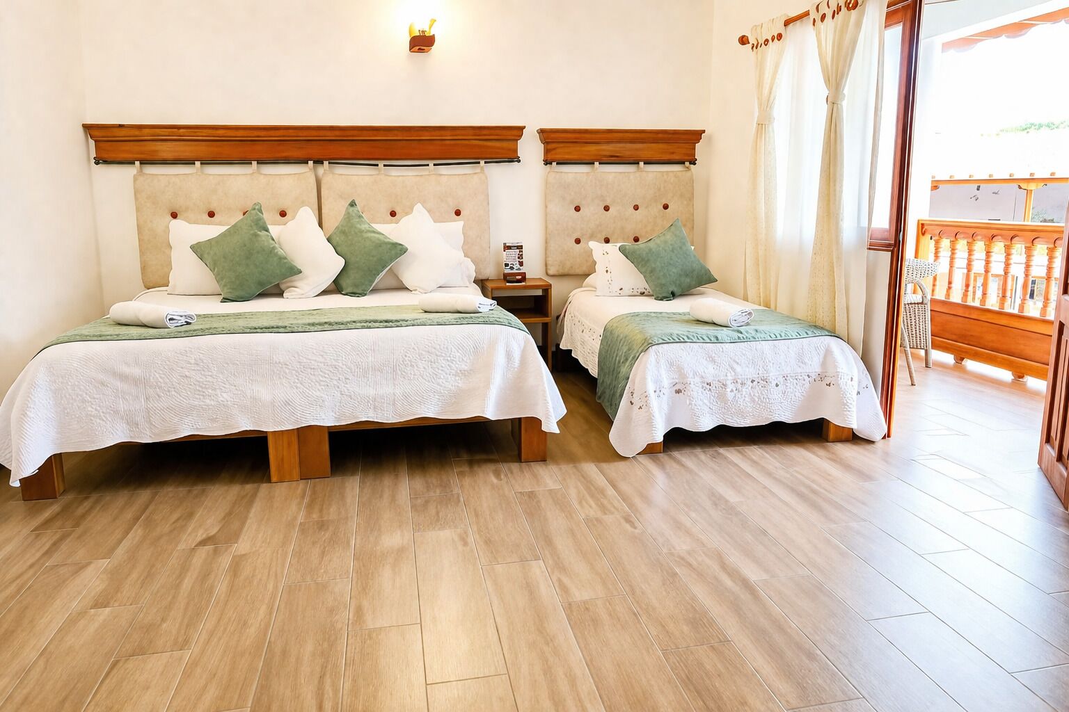 A double room with two beds, wooden headboards, a nightstand, a small table, and a view of a balcony.