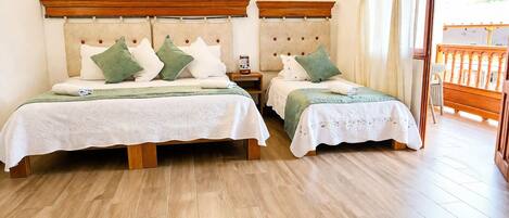 A double room with two beds, wooden headboards, a nightstand, a small table, and a view of a balcony.