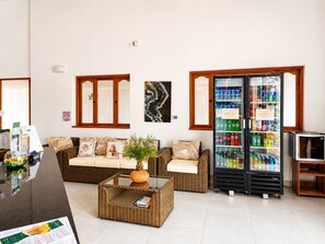 Un espace d’accueil comprenant un canapé, une table basse, un réfrigérateur rempli de boissons et un téléviseur posé sur un meuble.