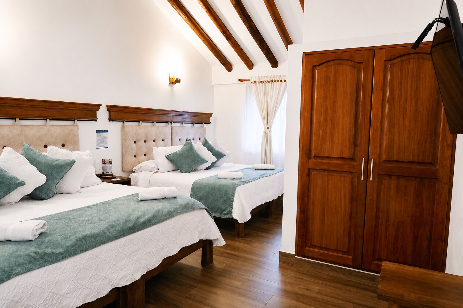 A hotel room with two beds, wooden headboards, a large wardrobe, and a ceiling with wooden beams.