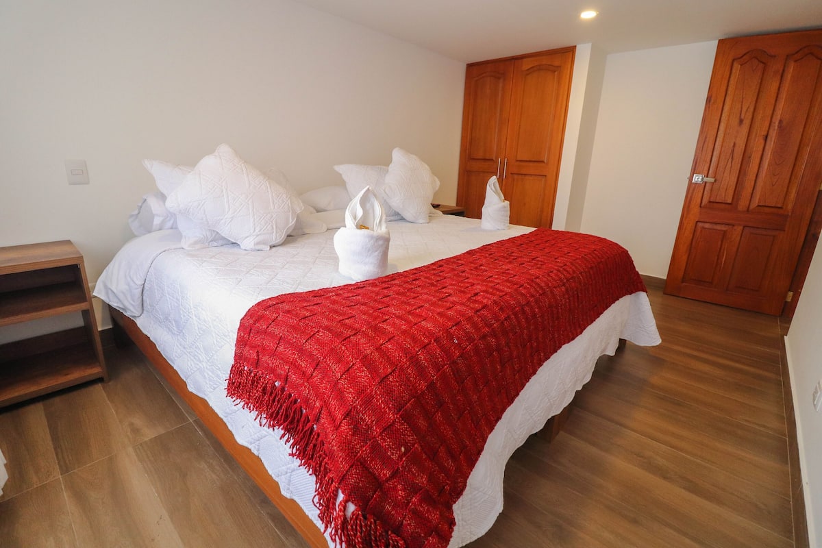 Ein Schlafzimmer mit einem Bett, weißen Kissen, einer roten Decke, Holzboden und einem Holzschrank.
