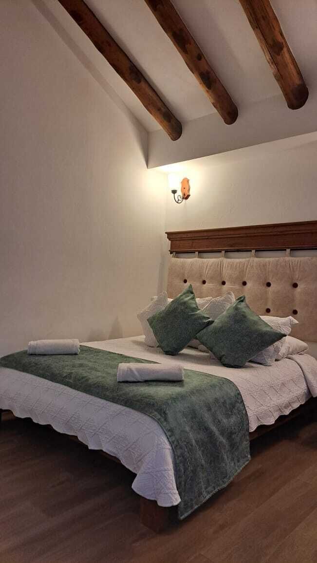 A bedroom with a wooden ceiling, a bed with green and white bedding, and a wall-mounted light fixture.