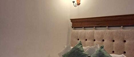 A bedroom with a wooden ceiling, a bed with green and white bedding, and a wall-mounted light fixture.