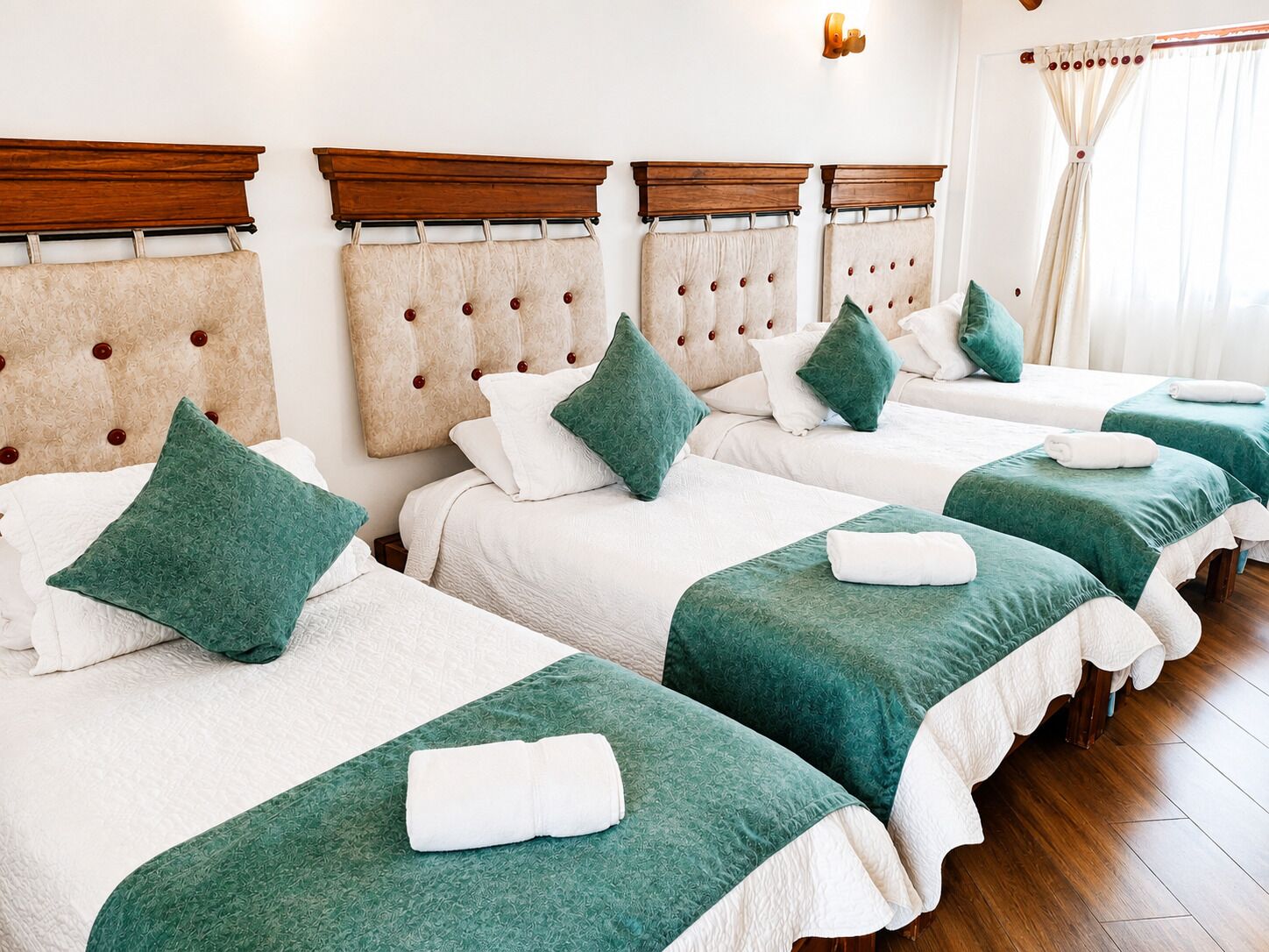 Habitación de hotel con cuatro camas, cada una con colcha verde y ropa de cama blanca, cabeceros de madera y suelo de madera.