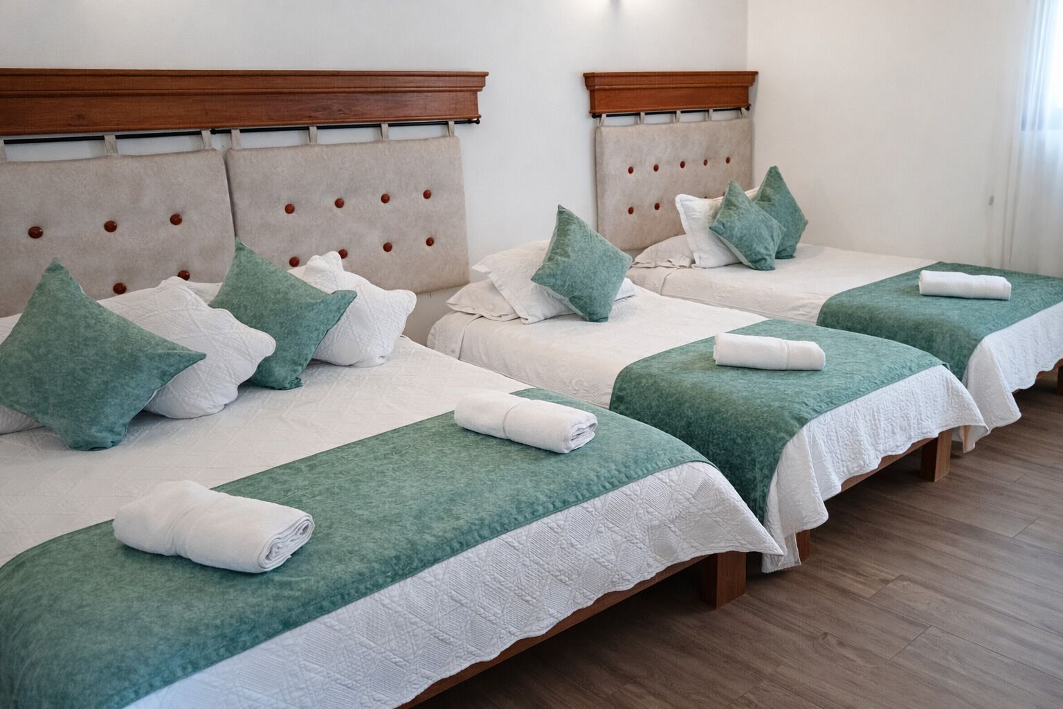 Four single beds with headboards, green bedspreads, and white linens.