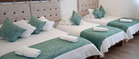 Four single beds with headboards, green bedspreads, and white linens.