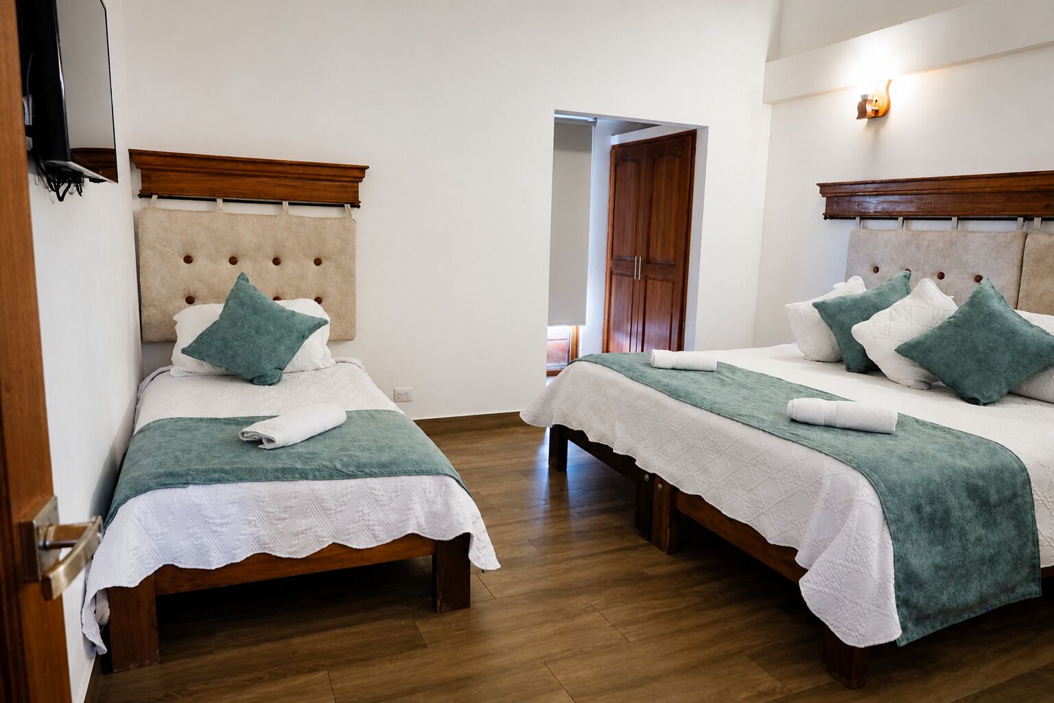 A hotel room with two beds, each with a headboard, a wooden floor, and a door leading to another room.