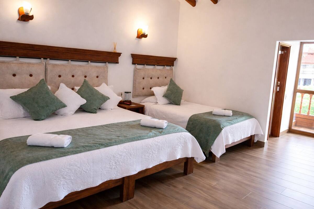 Ein Hotelzimmer mit zwei Betten, Holz-Kopfteilen, weißer Bettwäsche, grünen Zierkissen und Holzboden.