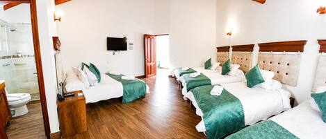 A hotel room with a wooden floor, a TV mounted on the wall, and a bed with green bedding.