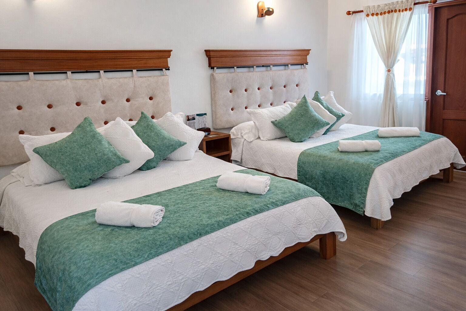 Dos camas dobles con cabeceros, ropa de cama verde y blanca, y piso de madera.