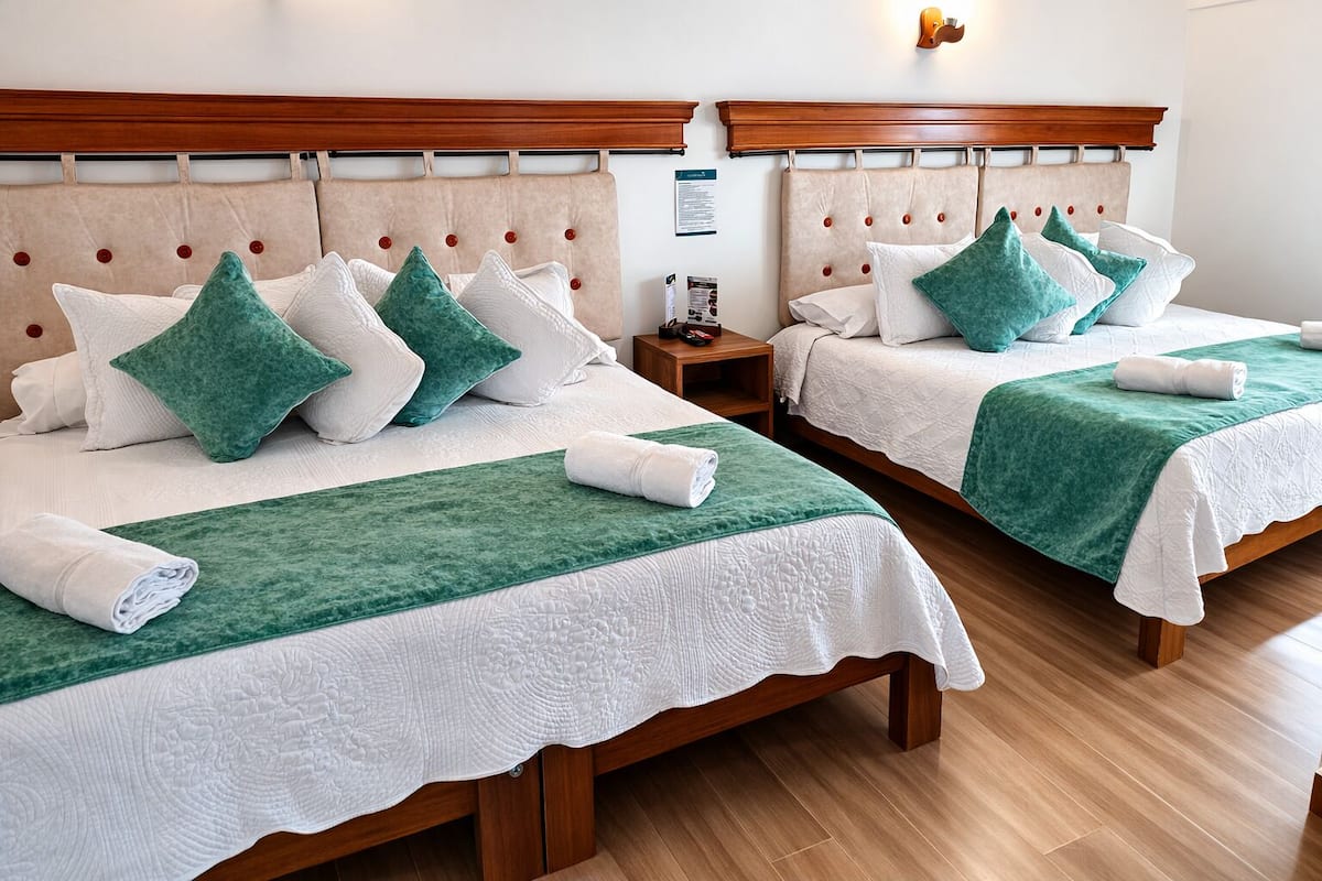Ein Hotelzimmer mit zwei Betten, jeweils mit einem Holzkopfstück, weißer Bettwäsche und grünen Zierkissen.