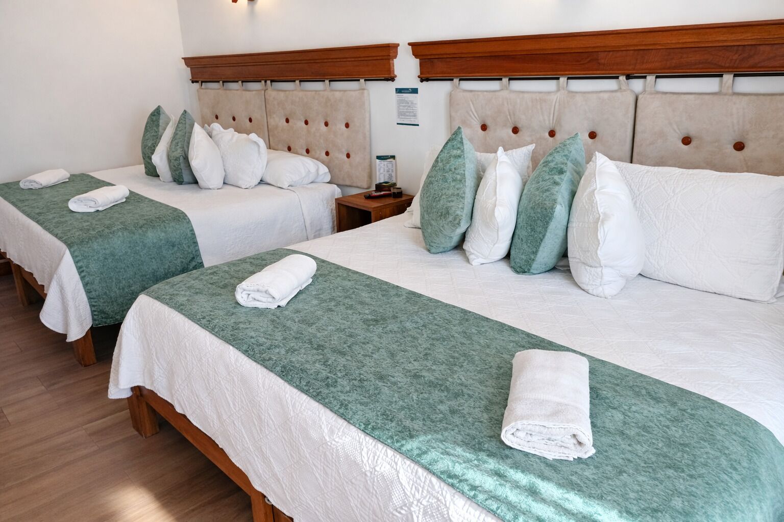 Habitación de hotel con dos camas, cada una con cubrecama verde y ropa de cama blanca, y cabeceros de madera.