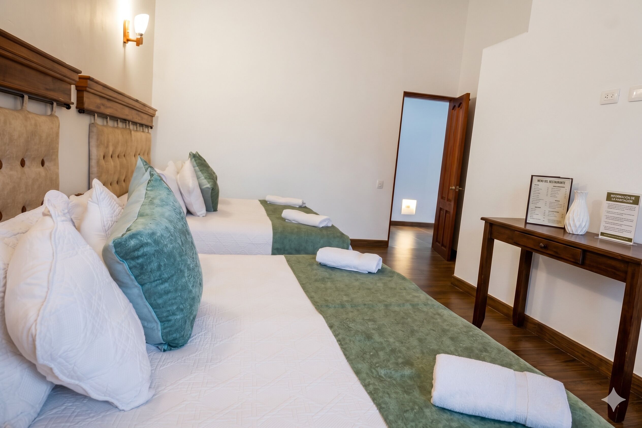 A hotel room with two beds, a wooden headboard, a green throw blanket, a wooden nightstand, and a mirror.