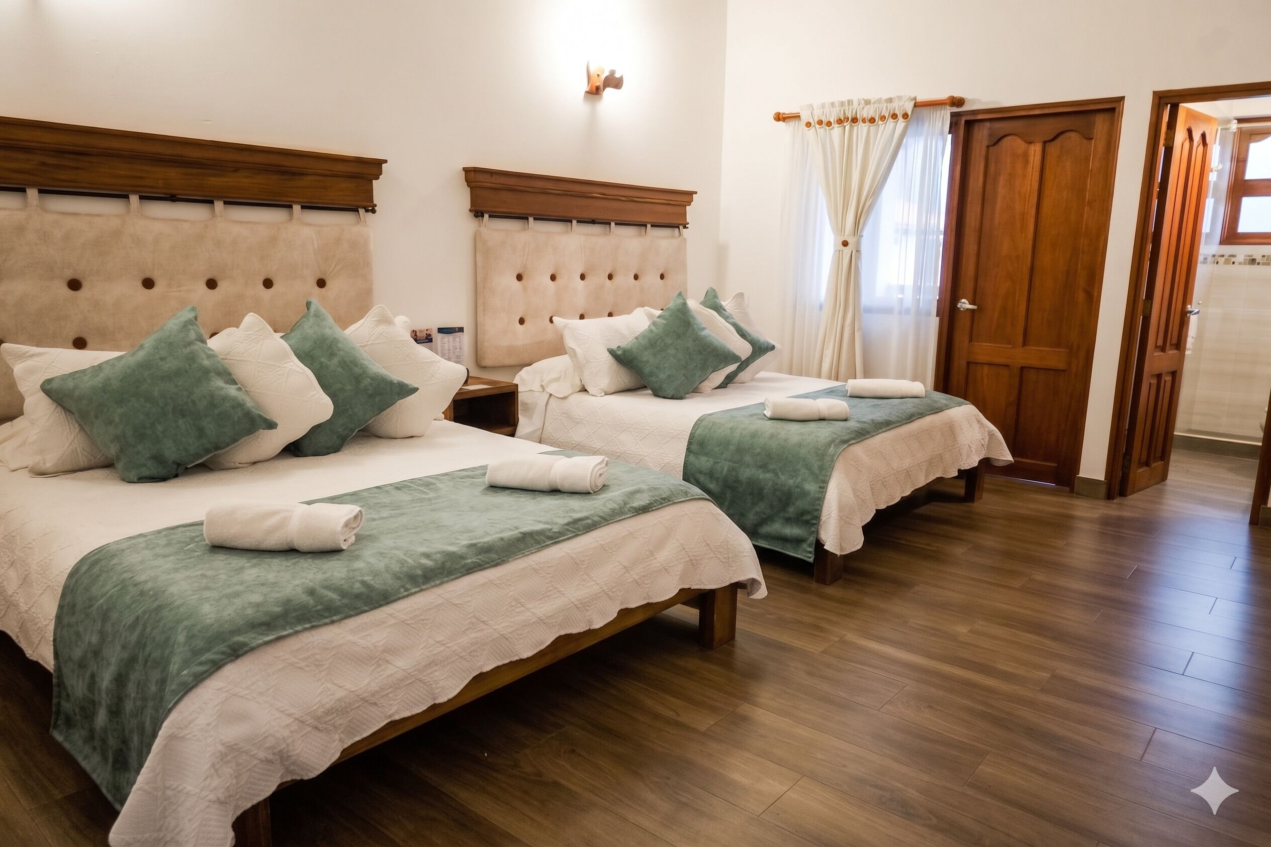 Habitación de hotel con dos camas, cabeceros de madera, una mesita de noche, una puerta de madera y una ventana con cortinas.