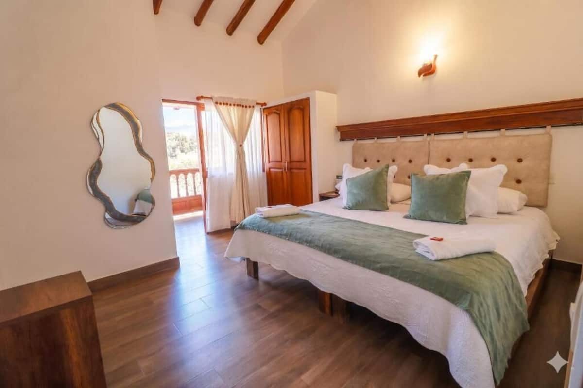 Ein Schlafzimmer mit Bett, Holzboden, Spiegel und einer Tür zu einem Außenbereich.