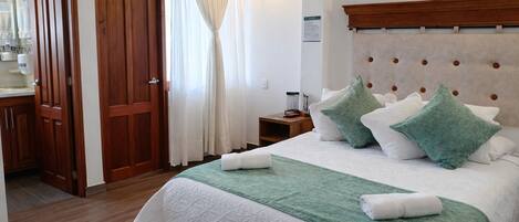 Una habitación de hotel con una cama, una puerta de madera, una mesita de noche y una ventana con cortinas.
