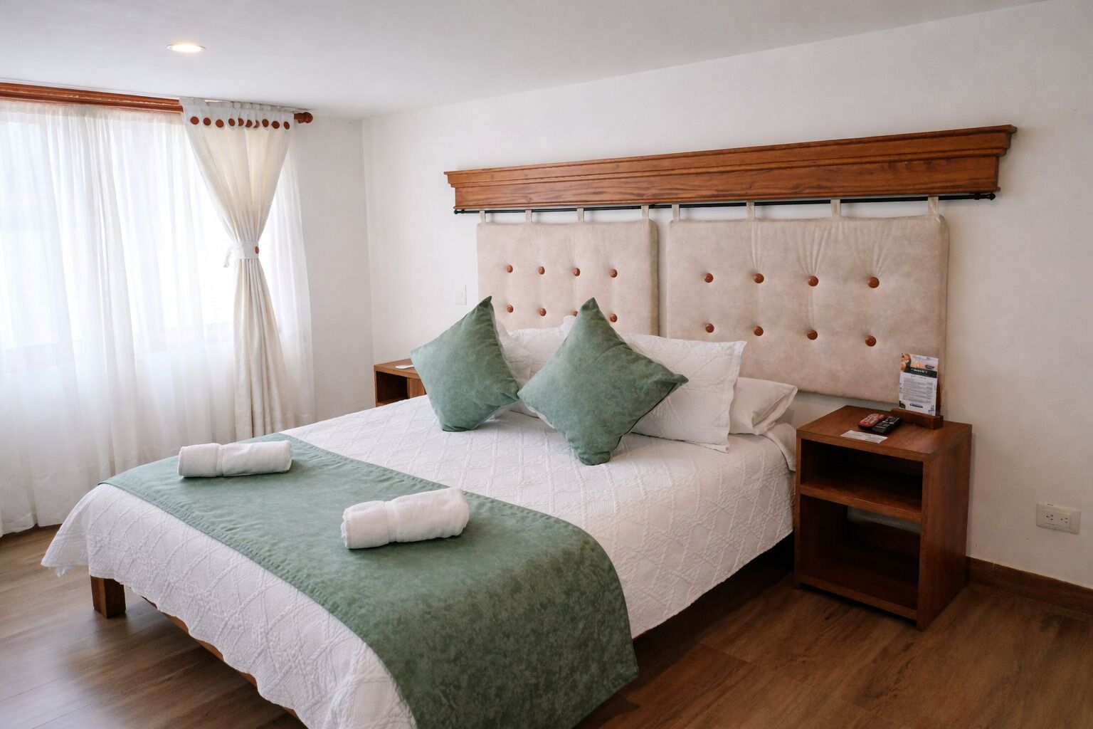 A neatly made bed with a green and white bedspread, two green pillows, and two white towels.