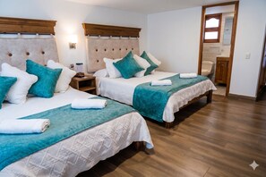 Une chambre d’hôtel avec deux lits, des têtes de lit en bois, du linge de lit blanc, des coussins décoratifs de couleur turquoise et un plancher en bois.