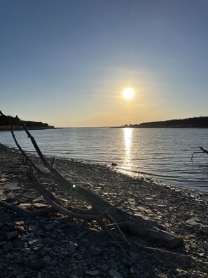 A rocky shoreline with a calm body of water reflecting the sun. - Country home with lake access and game room. (Milford)
